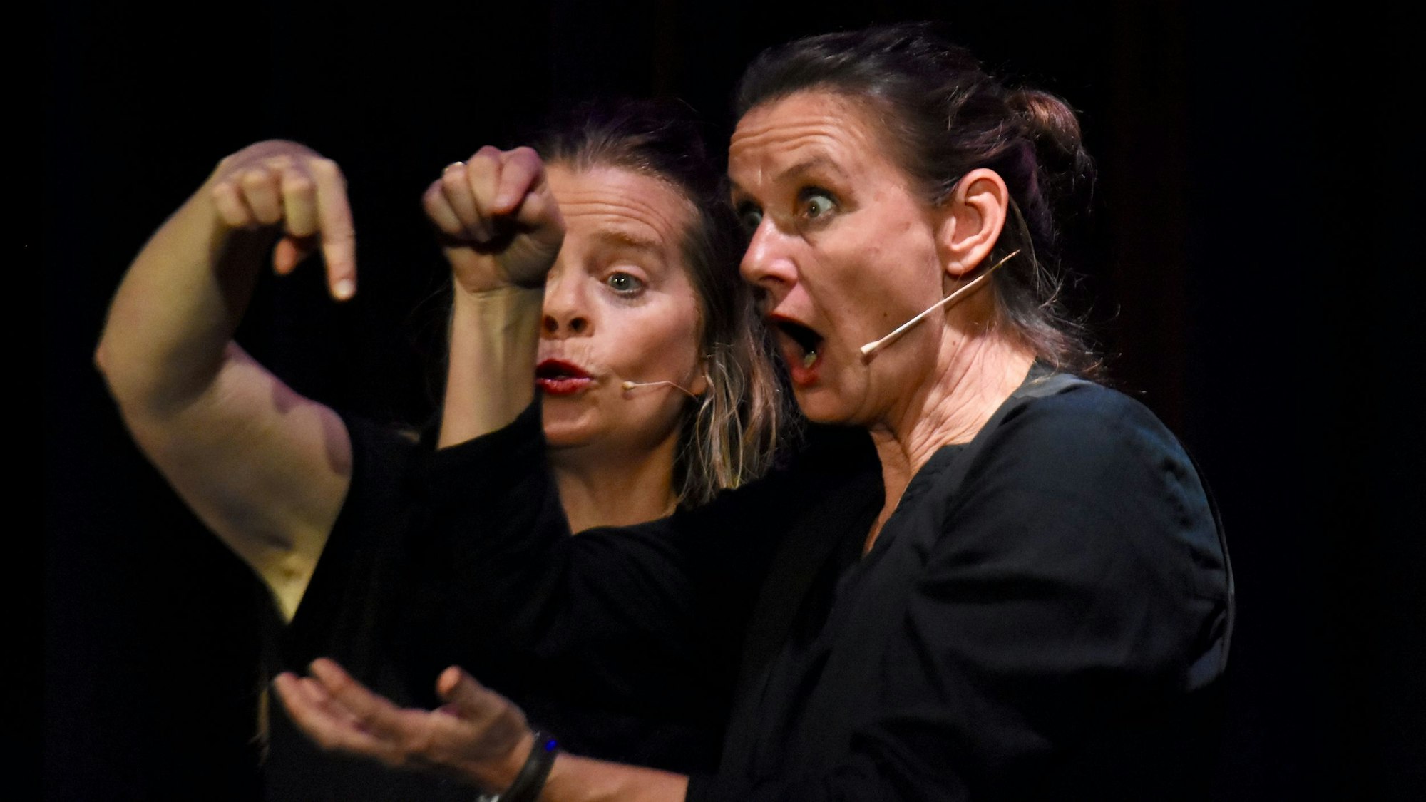 Zwei Frauen gestikulieren vor einem schwarzem Hintergund.