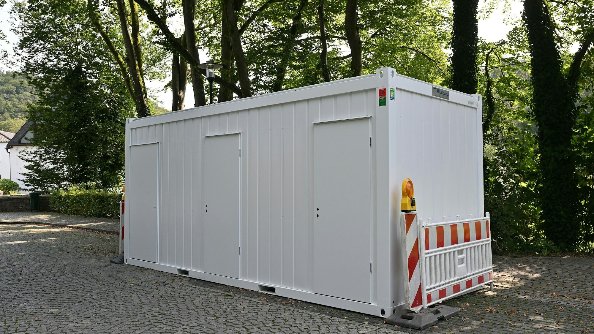 Ein weißer Toilettencontainer steht auf dem Parkplatz nahe dem Altenberger Dom.