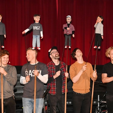 Die Musiker von Kasalla halten ihre Puppen vor dem Vorhang nach oben.