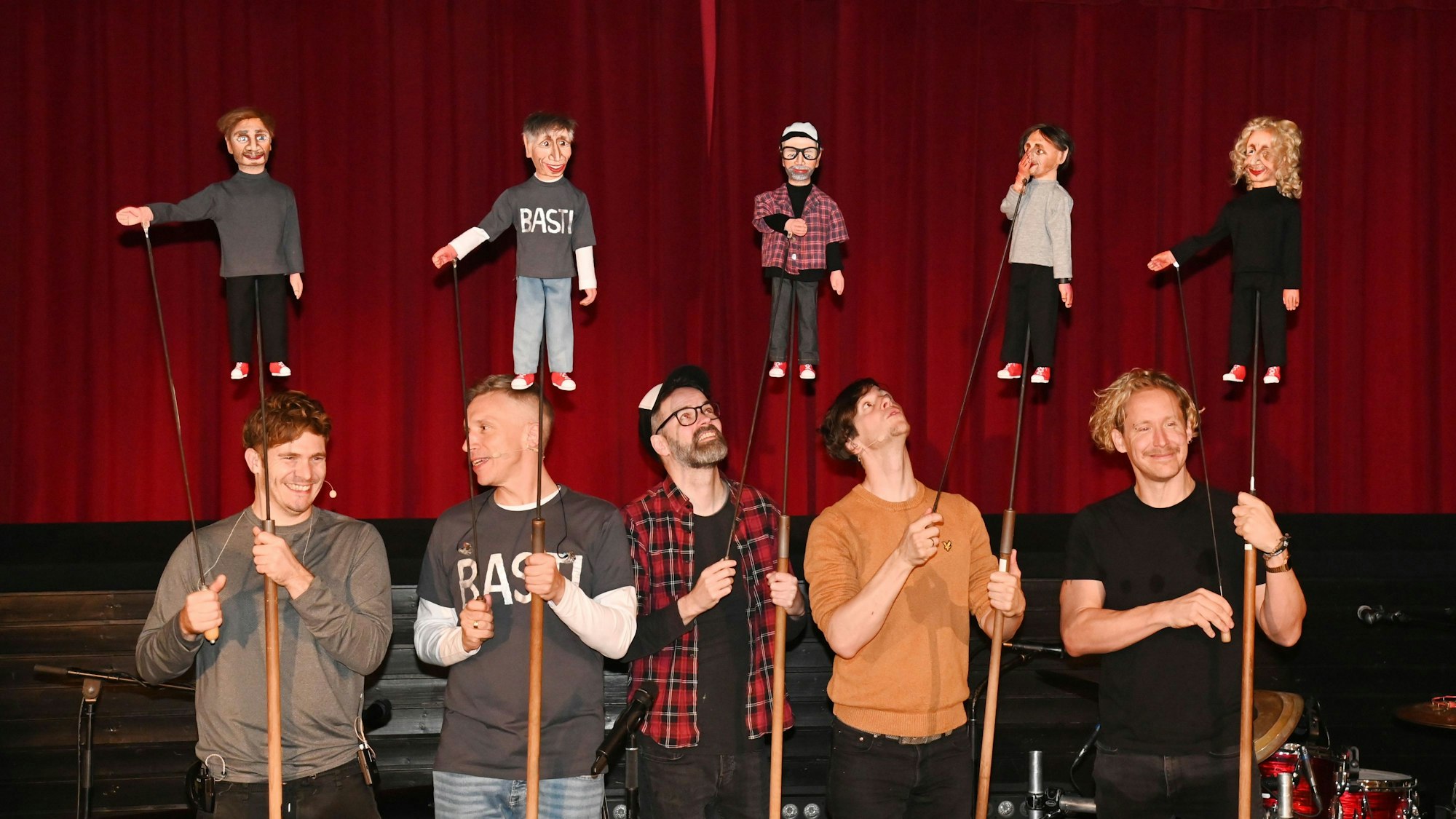 Die Musiker von Kasalla halten ihre Puppen vor dem Vorhang nach oben.