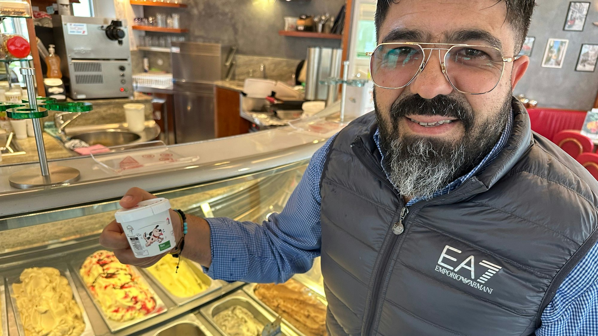Im Eiscafe Liotta Taormina in Hangelar steht Besitzer Alfredo Liotta vor der Eistheke und hält einen Becher Hundeeis in der Hand.
