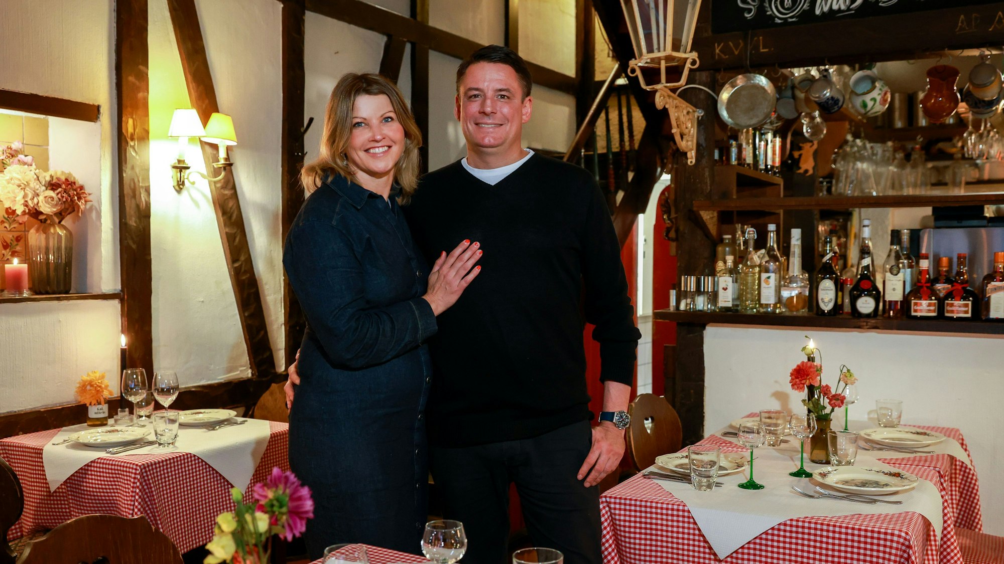 Die beiden stehen Arm in Arm im Restaurant und lachen in die Kamera.