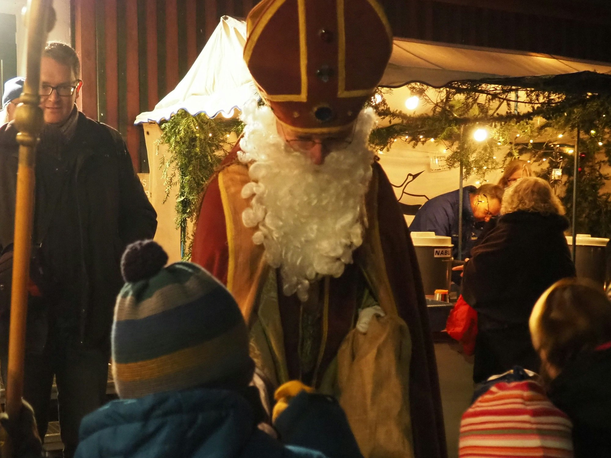 Ein Mann im Nikolauskostüm gibt Kindern auf dem Waldweihnachtsmarkt etwas aus dem Geschenkesack.