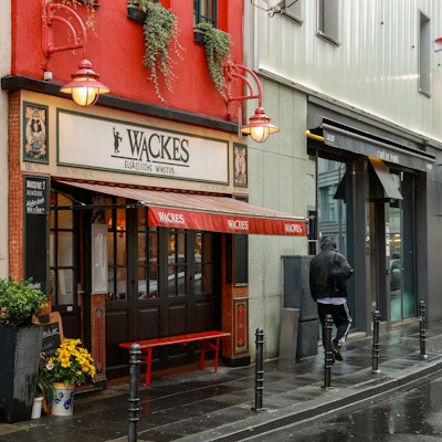 Das Restaurant "Wackes Elsässische Weinstube" ist von außen zu sehen: Eine Markise streckt sich über eine rot lackierte Bank vor dem Eingang.