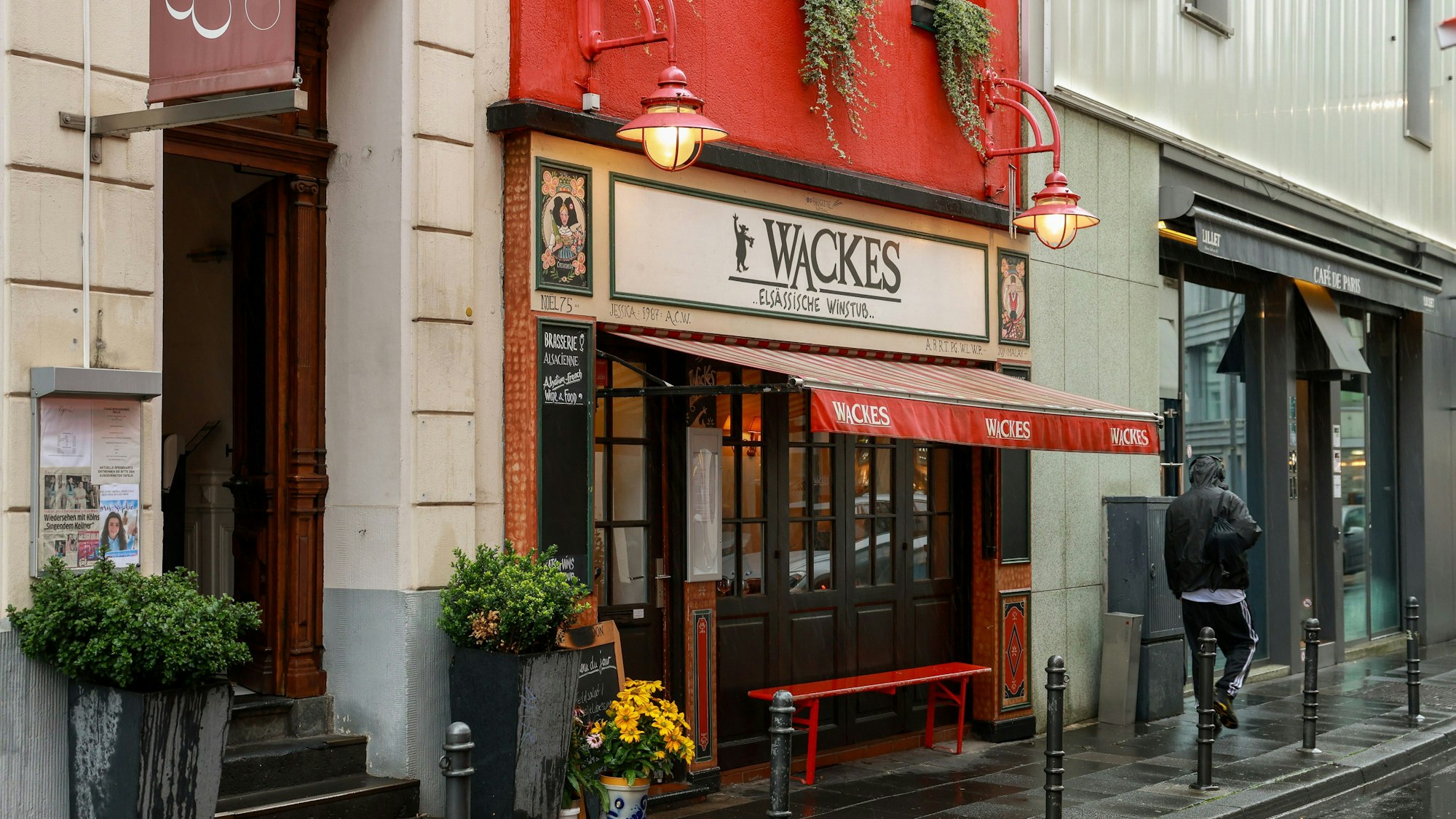 Das Restaurant "Wackes Elsässische Weinstube" ist von außen zu sehen: Eine Markise streckt sich über eine rot lackierte Bank vor dem Eingang.