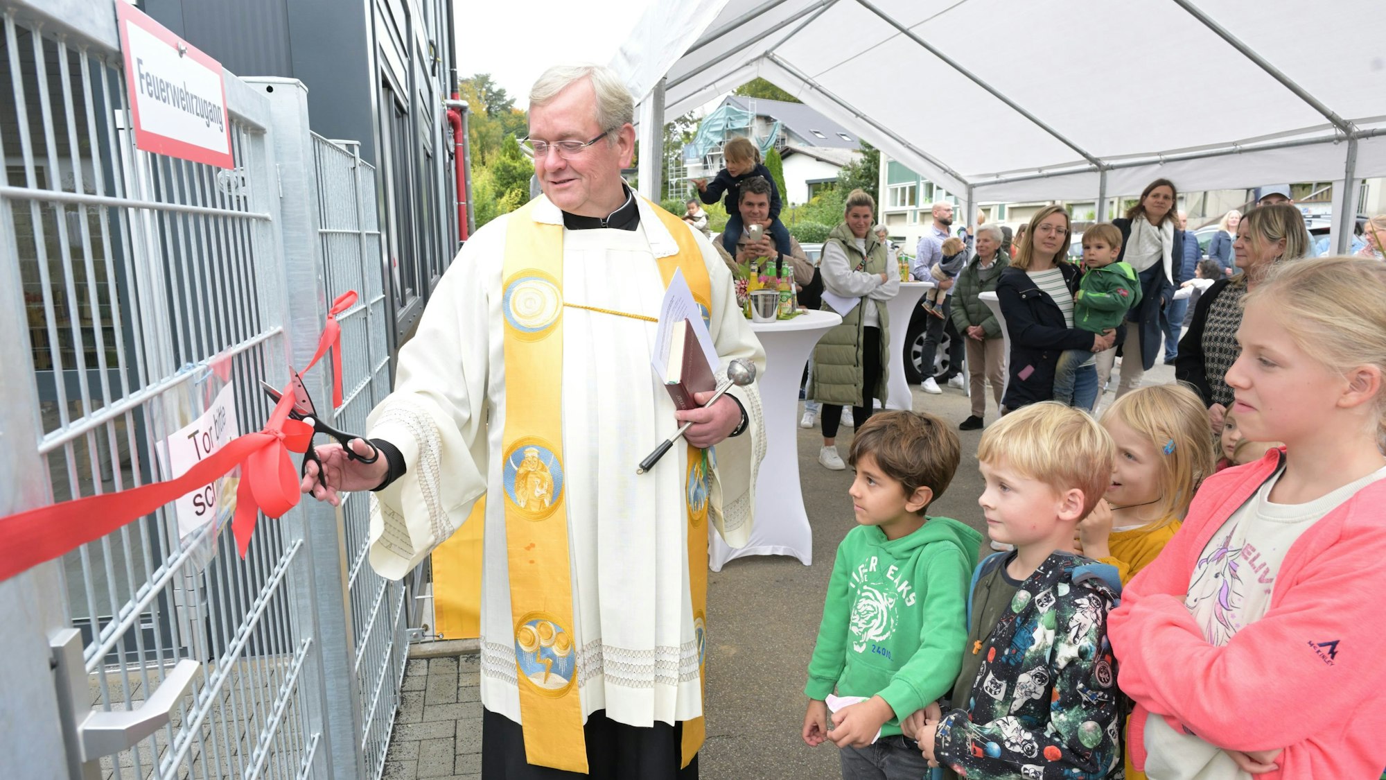 Pastor Franz Gerards segnete die neue Kita Himmelzelt in Rösrath-Forsbach. Er durchschnitt ein rotes Band und eröffnete so symbolisch den Container-Bau, in dem die Kita provisorisch unterkommt.
