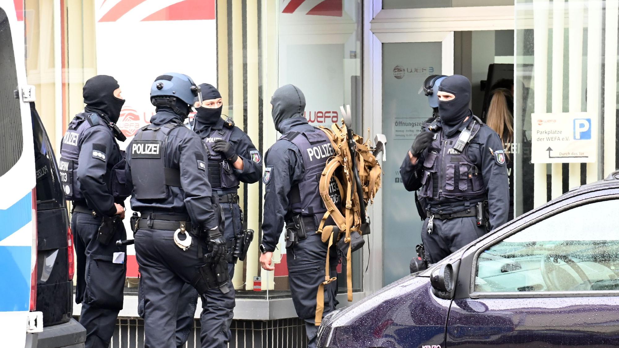 Vermummte Einsatzkräfte stehen im Zuge einer Razzia bei WEFA auf der Franz-Geuer-Straße in Ehrenfeld vor dem Gebäude.
