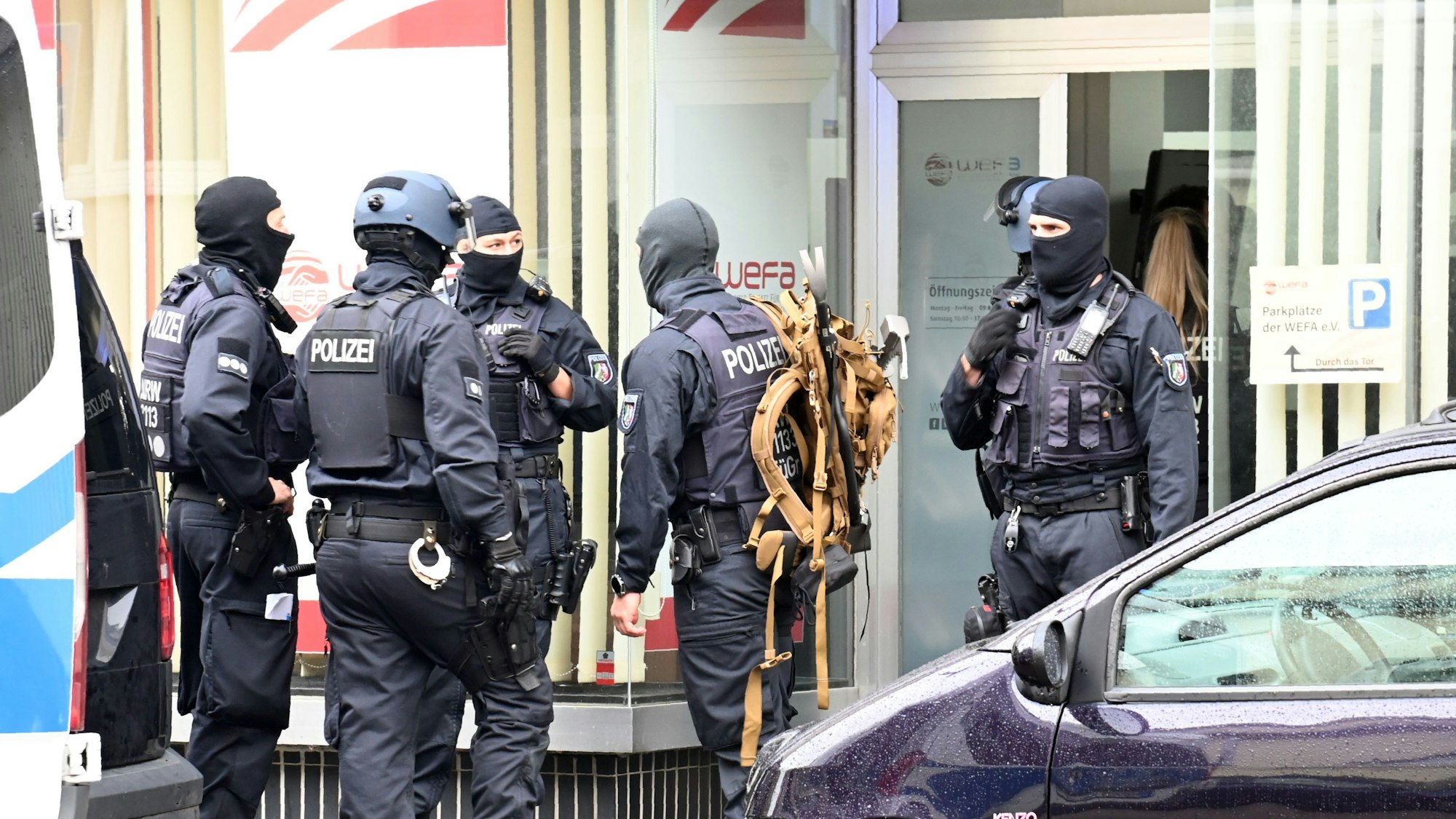 Vermummte Einsatzkräfte stehen im Zuge einer Razzia bei WEFA auf der Franz-Geuer-Straße in Ehrenfeld vor dem Gebäude.