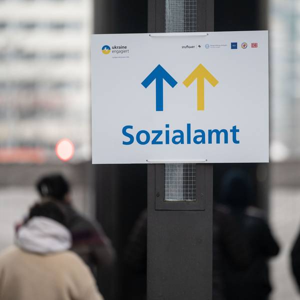 Geflüchtete stehen vor einem Schild mit dem Aufdruck Sozialamt