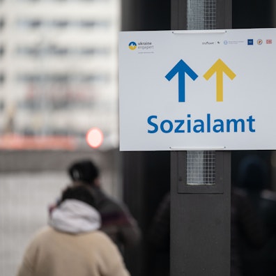 Geflüchtete stehen vor einem Schild mit dem Aufdruck Sozialamt