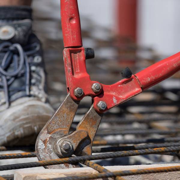 Mit einem Bolzenschneider schneiden Handwerker auf dem Rohbau eines Mehrfamilienhauses Stahlmatten auf die richtige Größe.