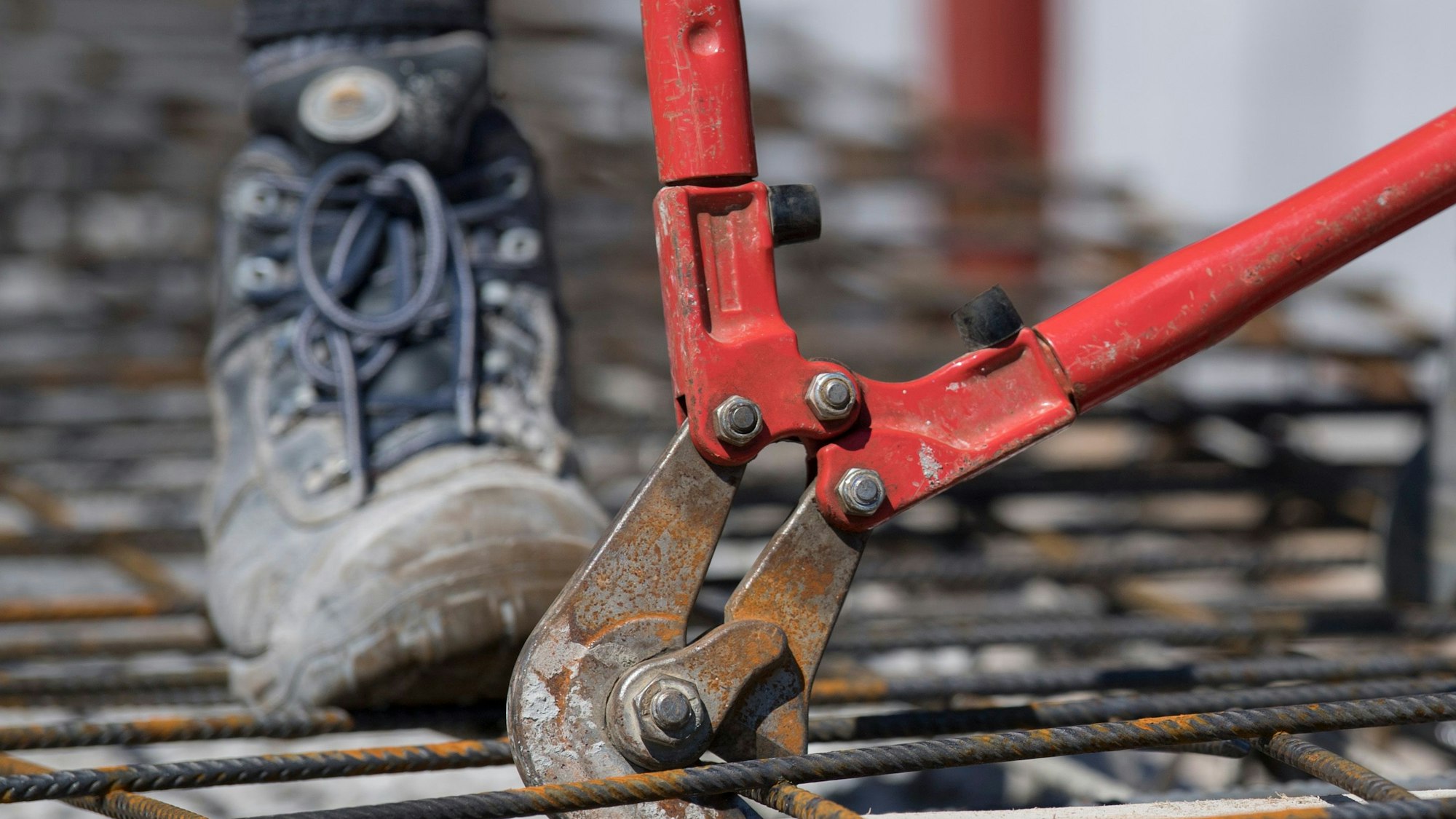 Mit einem Bolzenschneider schneiden Handwerker auf dem Rohbau eines Mehrfamilienhauses Stahlmatten auf die richtige Größe.
