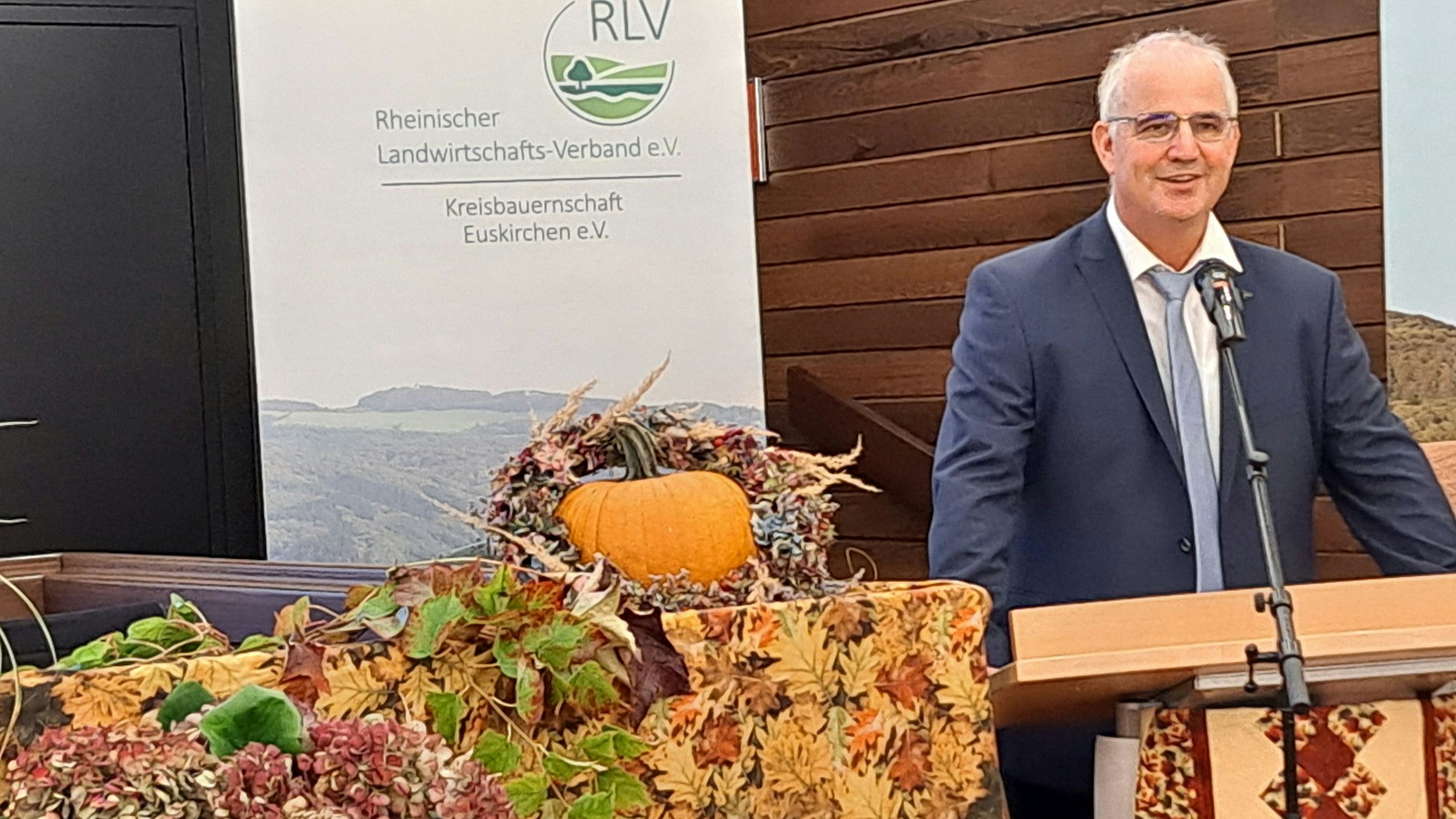 Helmut Dahmen steht am Rednerpult, neben ihm ist herbstliche Dekoration zu sehen.