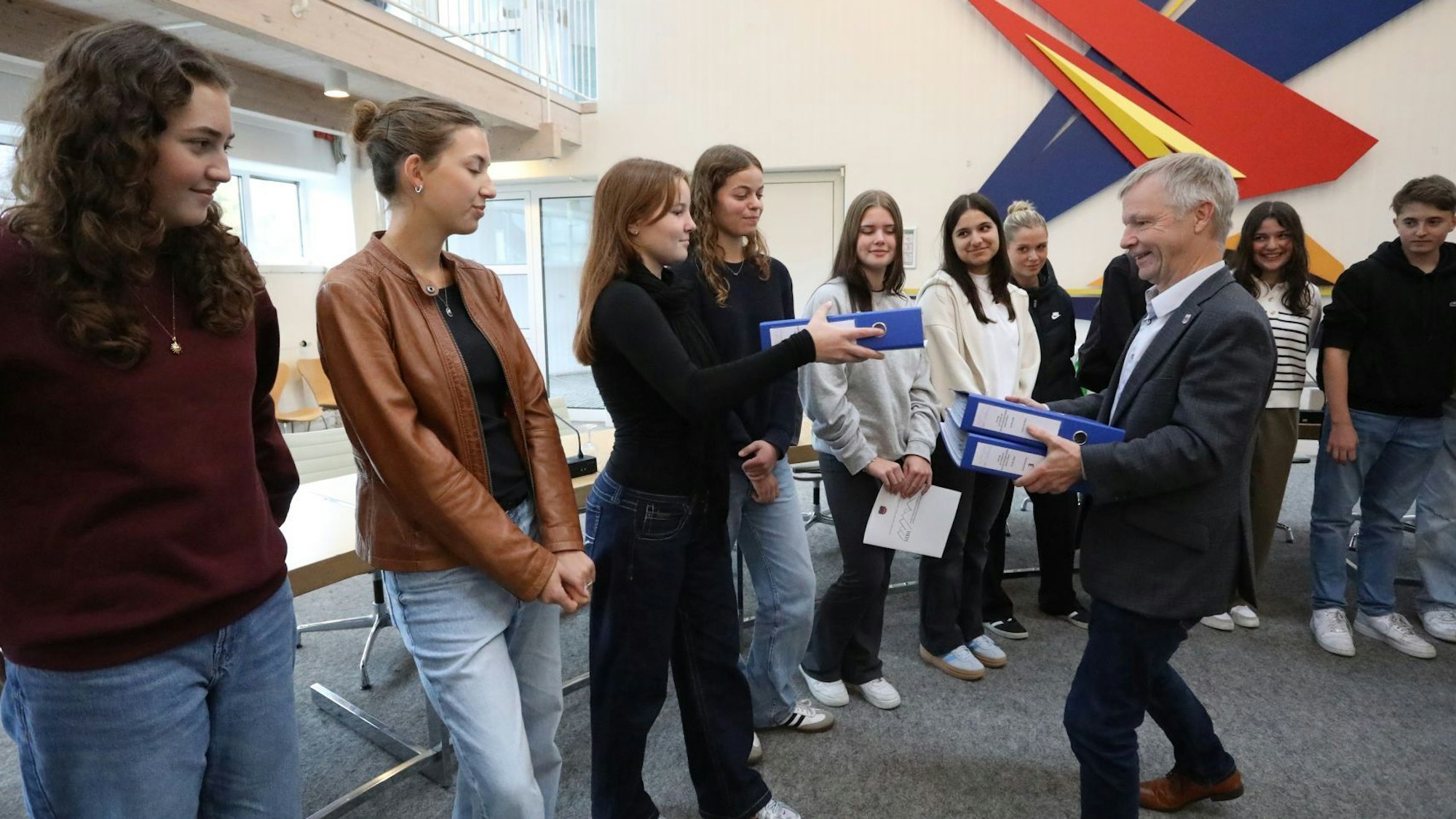 Eine Gruppe von jungen Leuten übergibt dem Bürgermeister drei blaue Aktenordner.