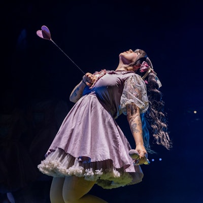 10.10.2024, Köln: Melanie Martinez trägt ein kurzes Rüschenkleid. Mit einer Hand hält sie einen Pfeil fest, der sie dem Anschein nach in die Brust getroffen hat.