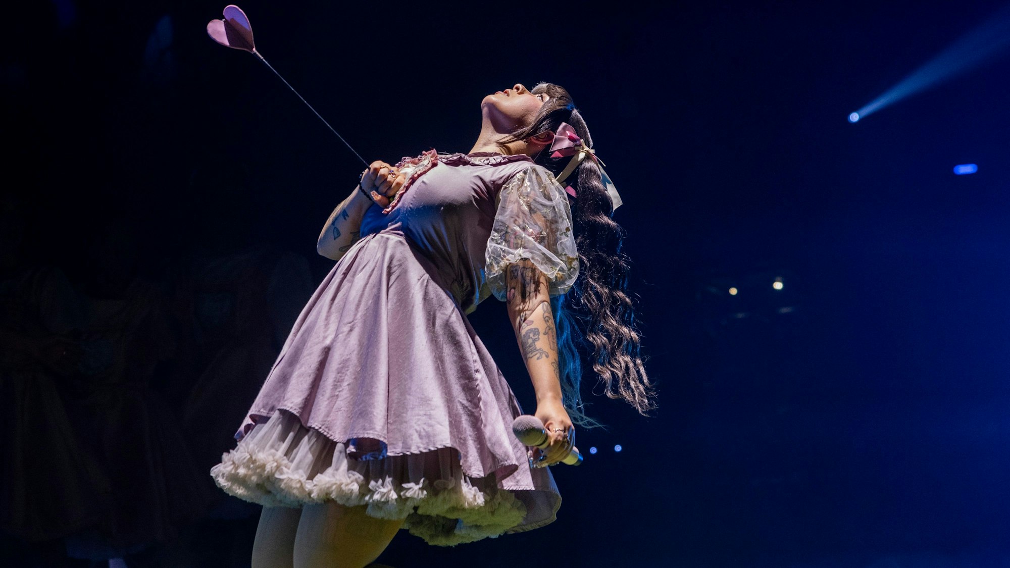 10.10.2024, Köln: Melanie Martinez trägt ein kurzes Rüschenkleid. Mit einer Hand hält sie einen Pfeil fest, der sie dem Anschein nach in die Brust getroffen hat.