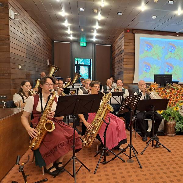 Musikerinnen und Musiker spielen auf Blasinstrumenten, rechts davon liegen Feldfrüchte und Äpfel als Deko.