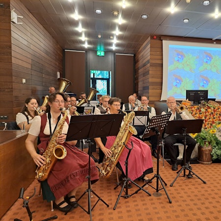 Musikerinnen und Musiker spielen auf Blasinstrumenten, rechts davon liegen Feldfrüchte und Äpfel als Deko.