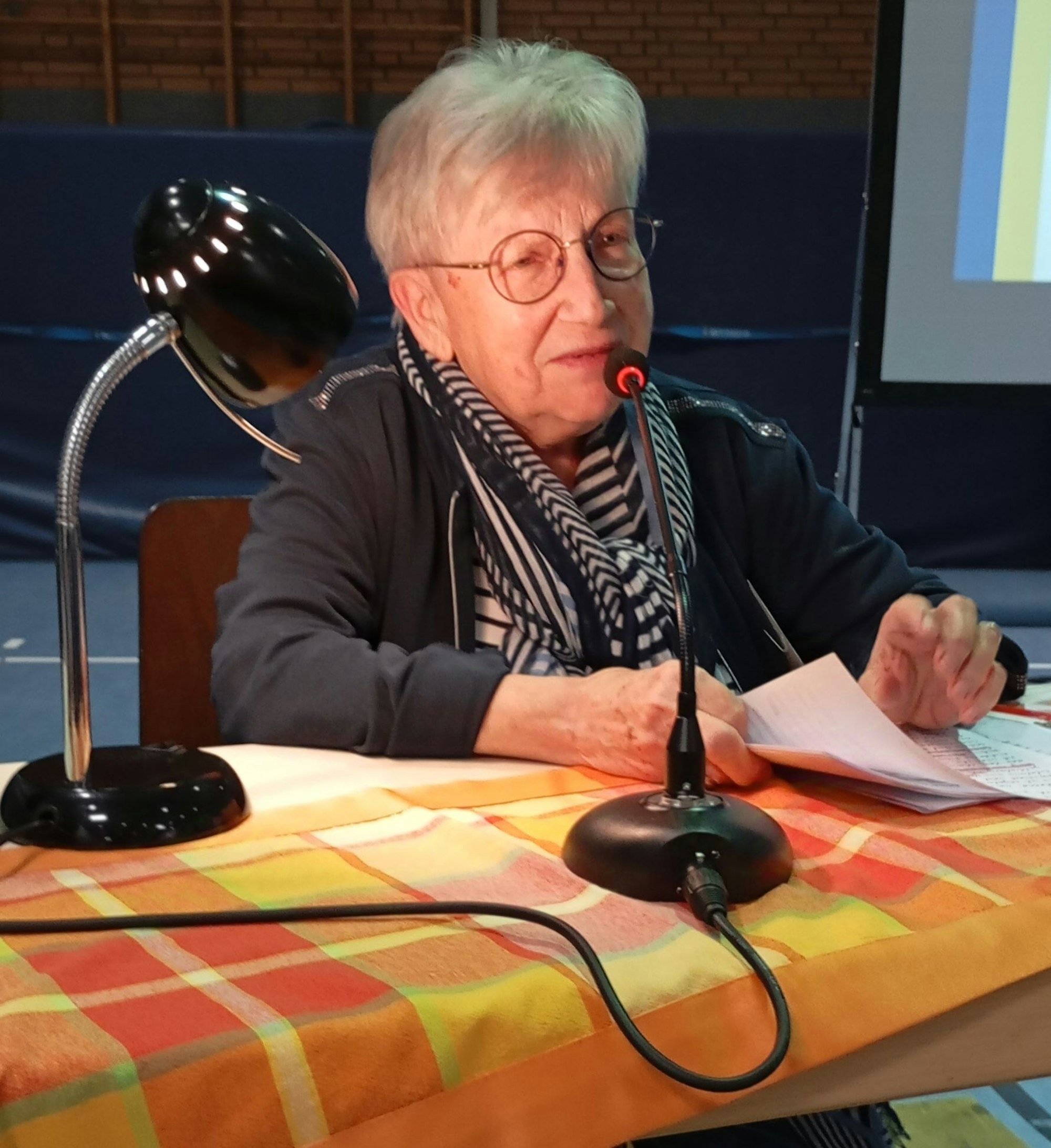 Das Bild zeigt eine Seniorin am Mikrofon.
