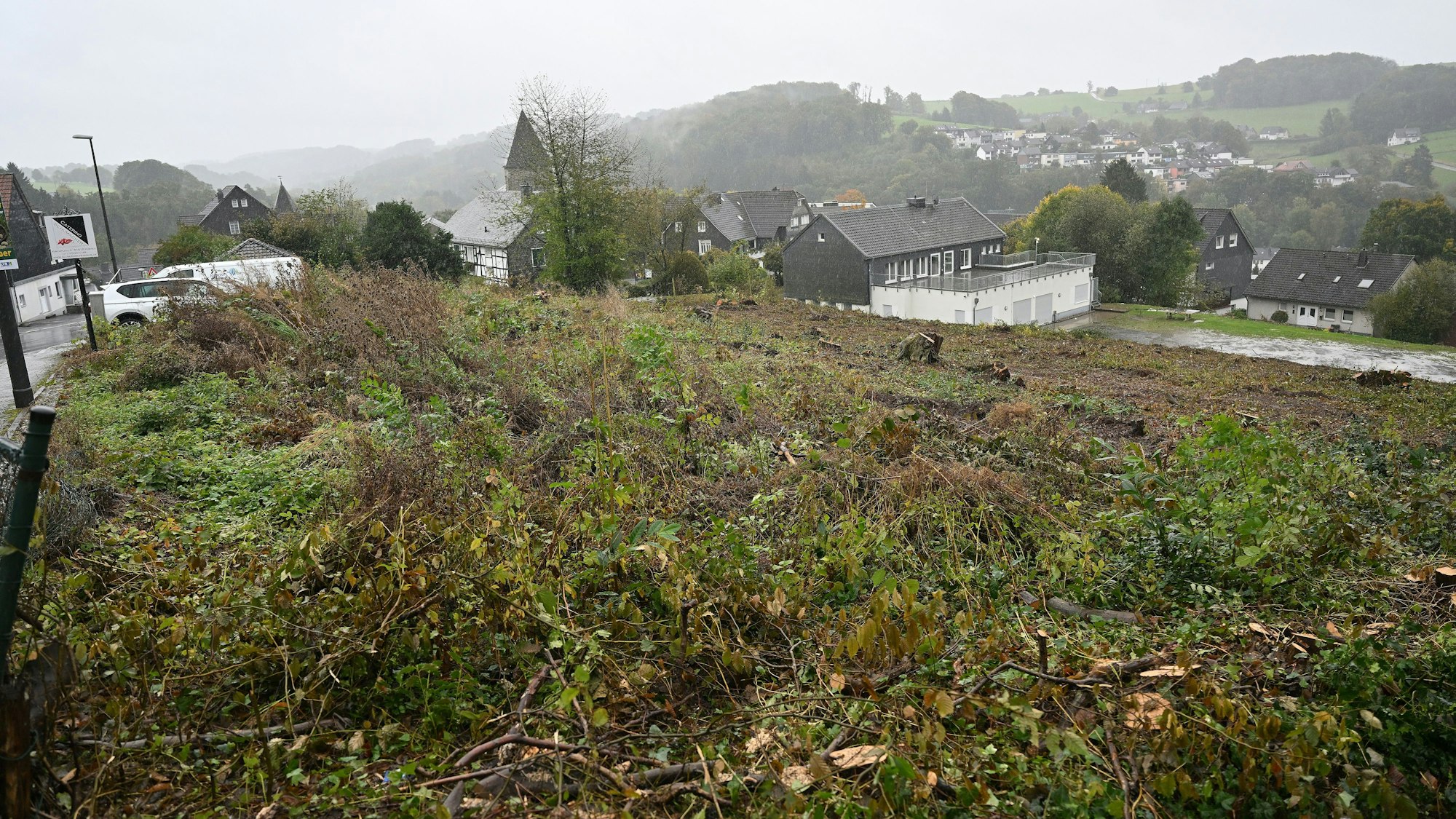 Ein abgeholztes Gelände am Hang der Bergstraße in Kürten. Im Hintergrund eine Kirche.