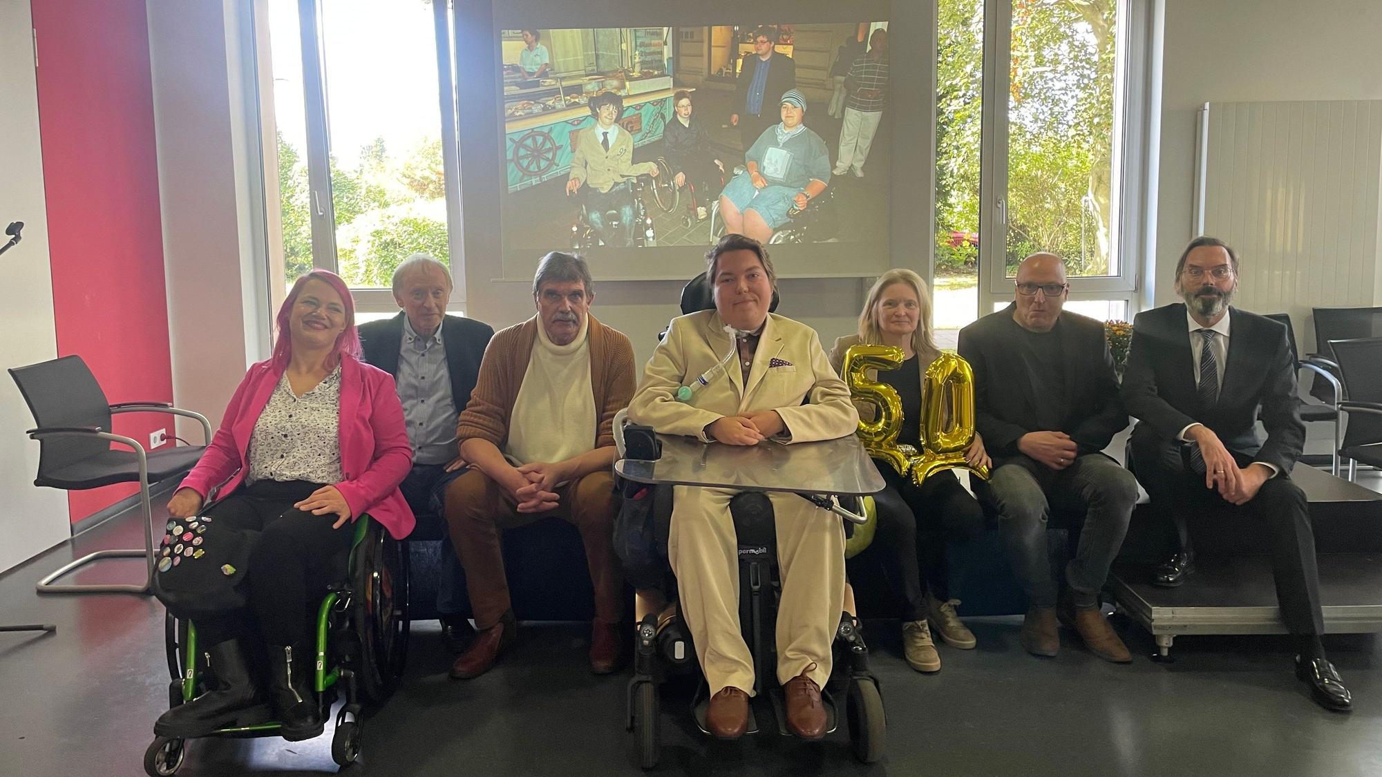 Das Foto zeigt eine Reihe von Besucherinnen und Besuchern der Jubiläumsfeier. Im Hintergrund die Projektion eines alten Fotos.