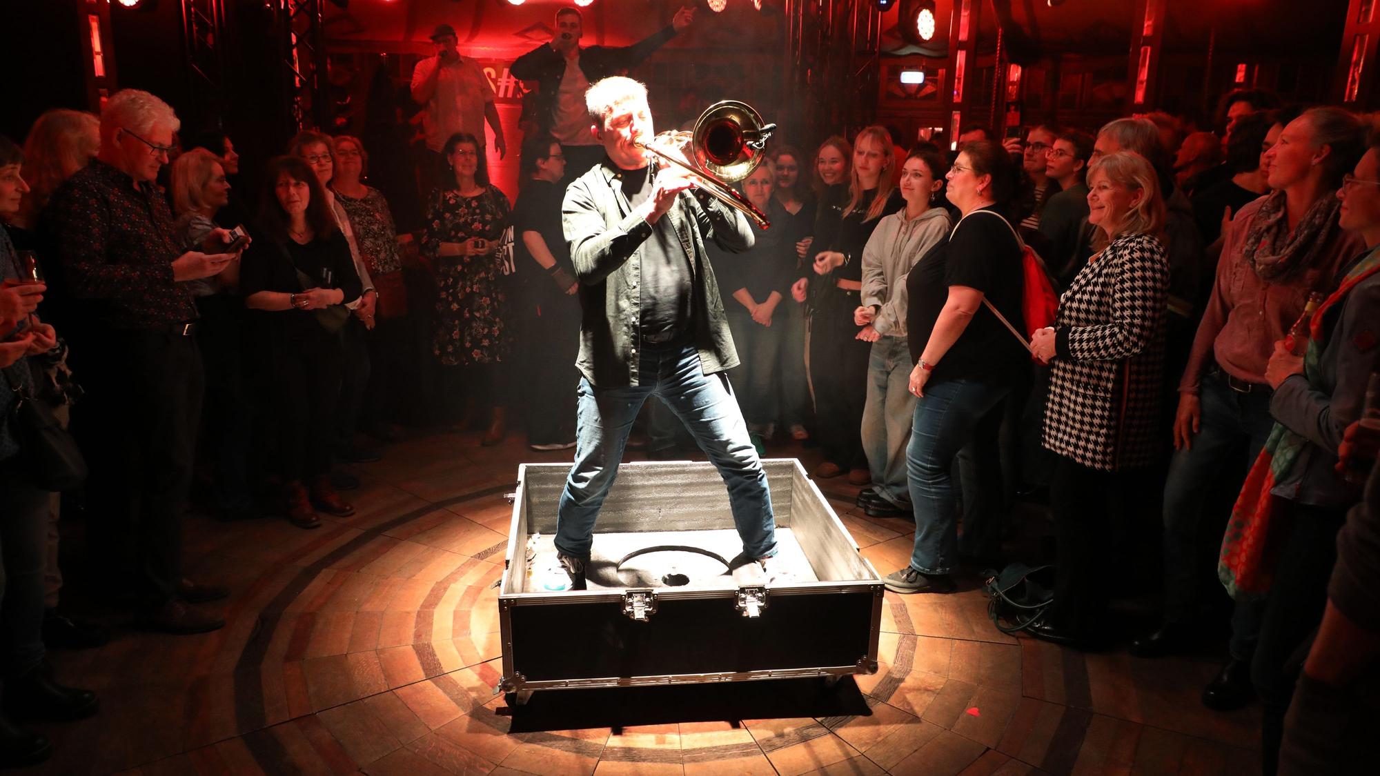 Ex-Wise-Guy Clemens Tewinkel steht mit Posaune im Scheinwerferkegel in einer Transportbox.