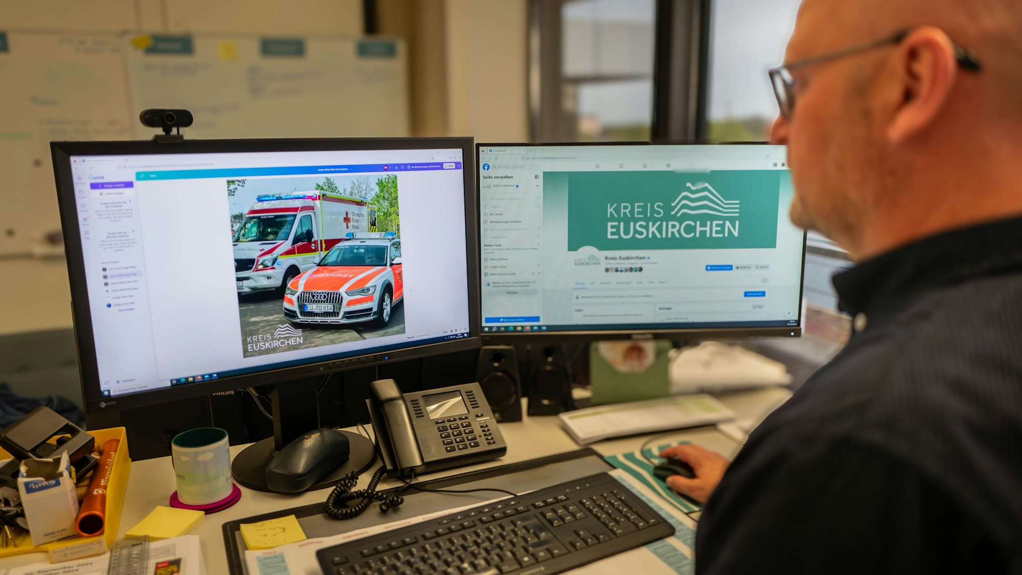 Ein Mann im schwarzen Hemd sitzt vor zwei Computerbildschirmen.