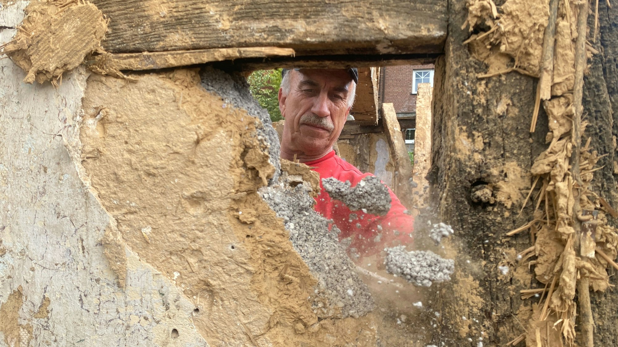 Ein Handwerker schlägt ein Loch in eine Lehm-Fachwerkwand.