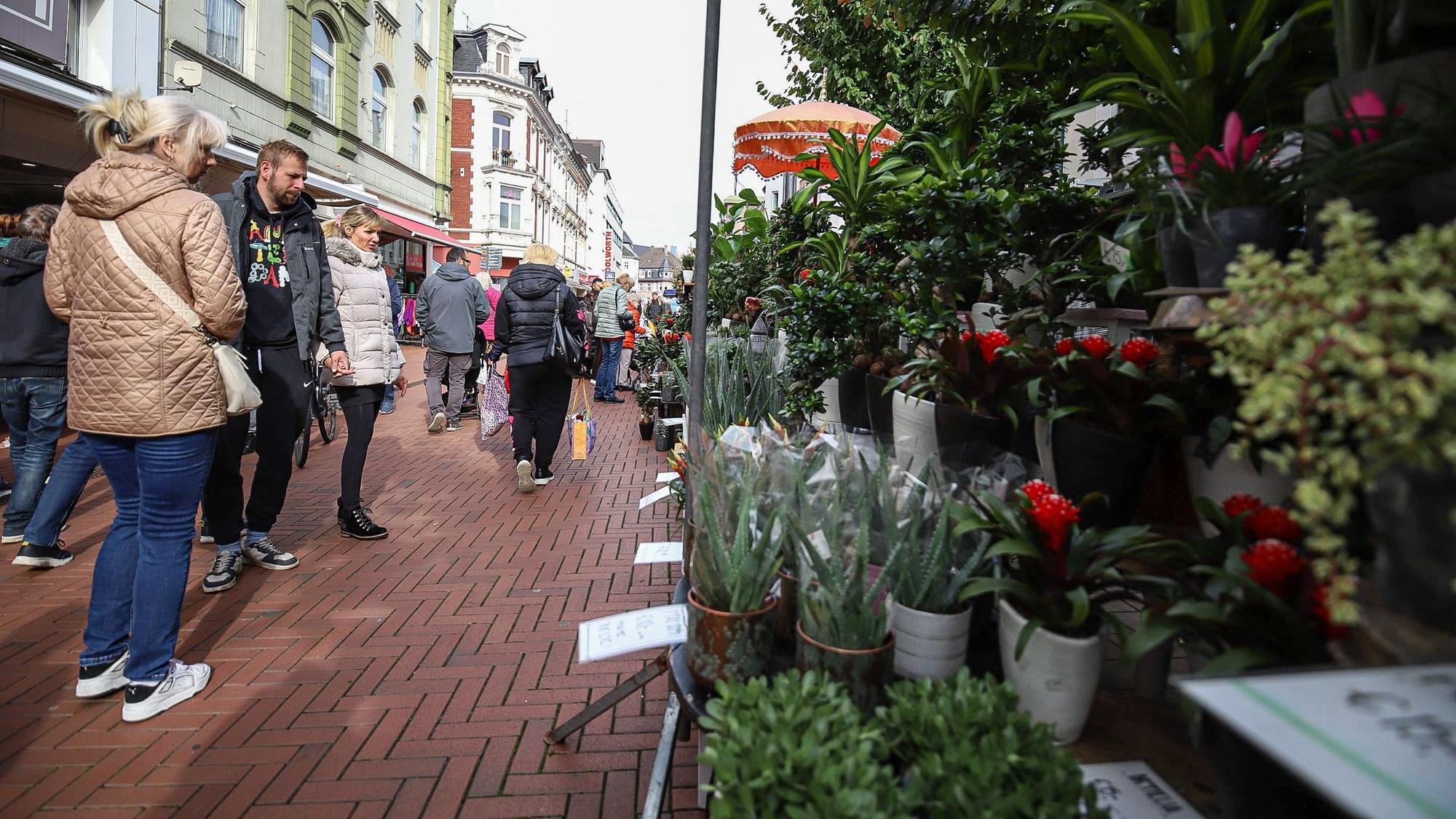 Menschen stehen vor einem Blumenstand in einer Fußgängerzone.