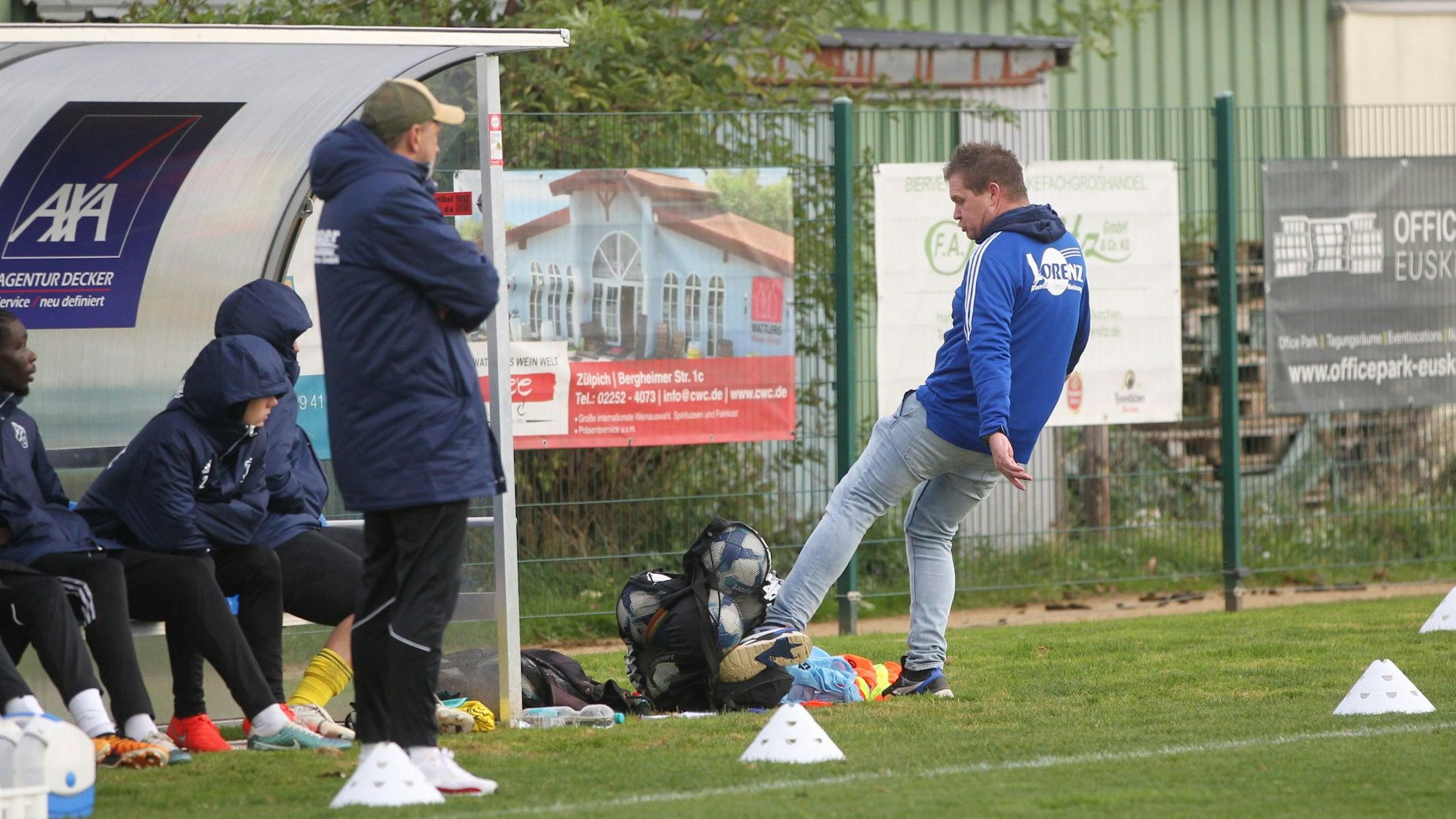 Der Trainer lässt seine Wut am Bällesack aus. Einige seiner Spieler schauen zu.