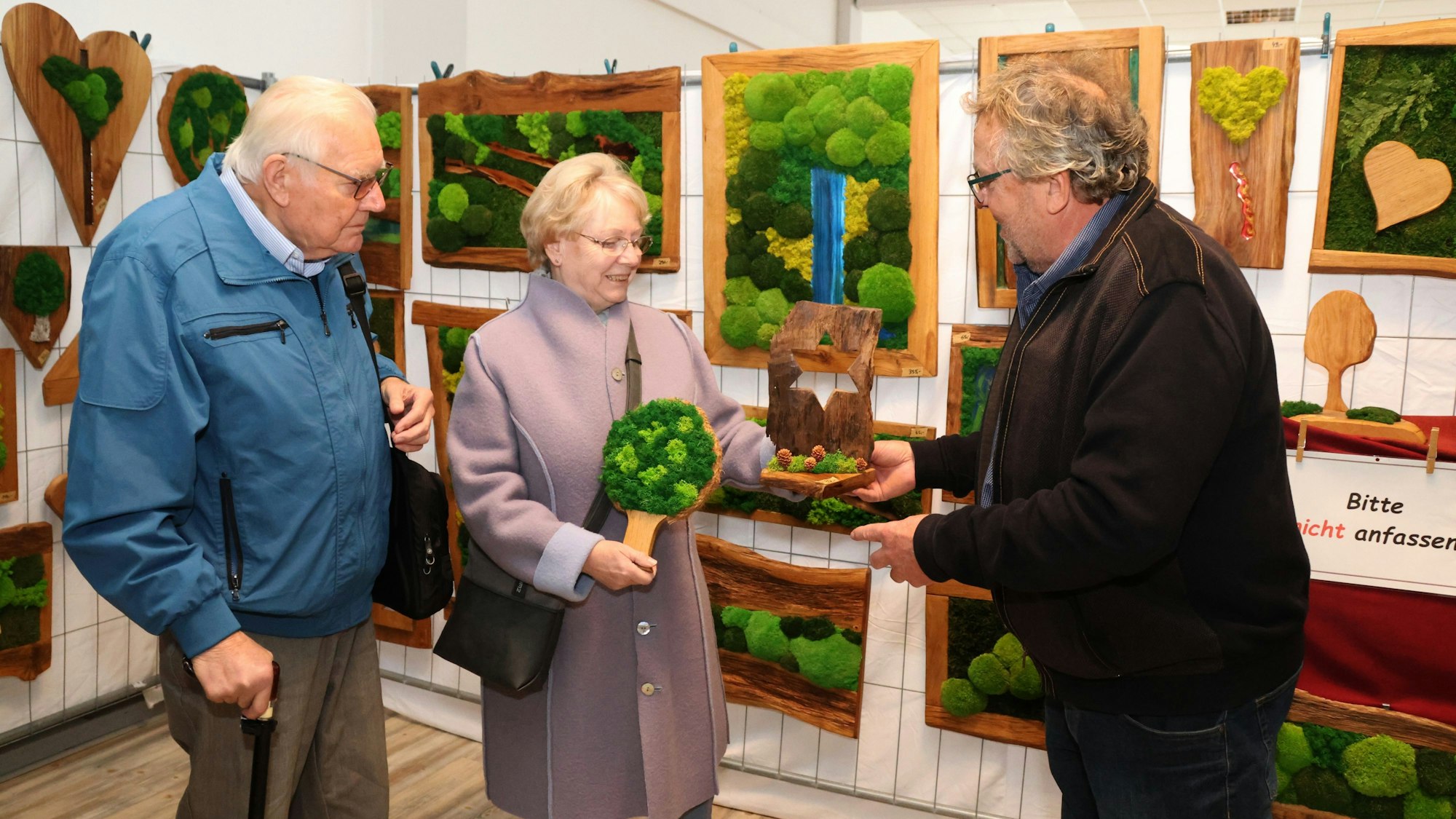 Ein Mann zeigt zwei Besuchern mit Moos bedeckte Objekte.