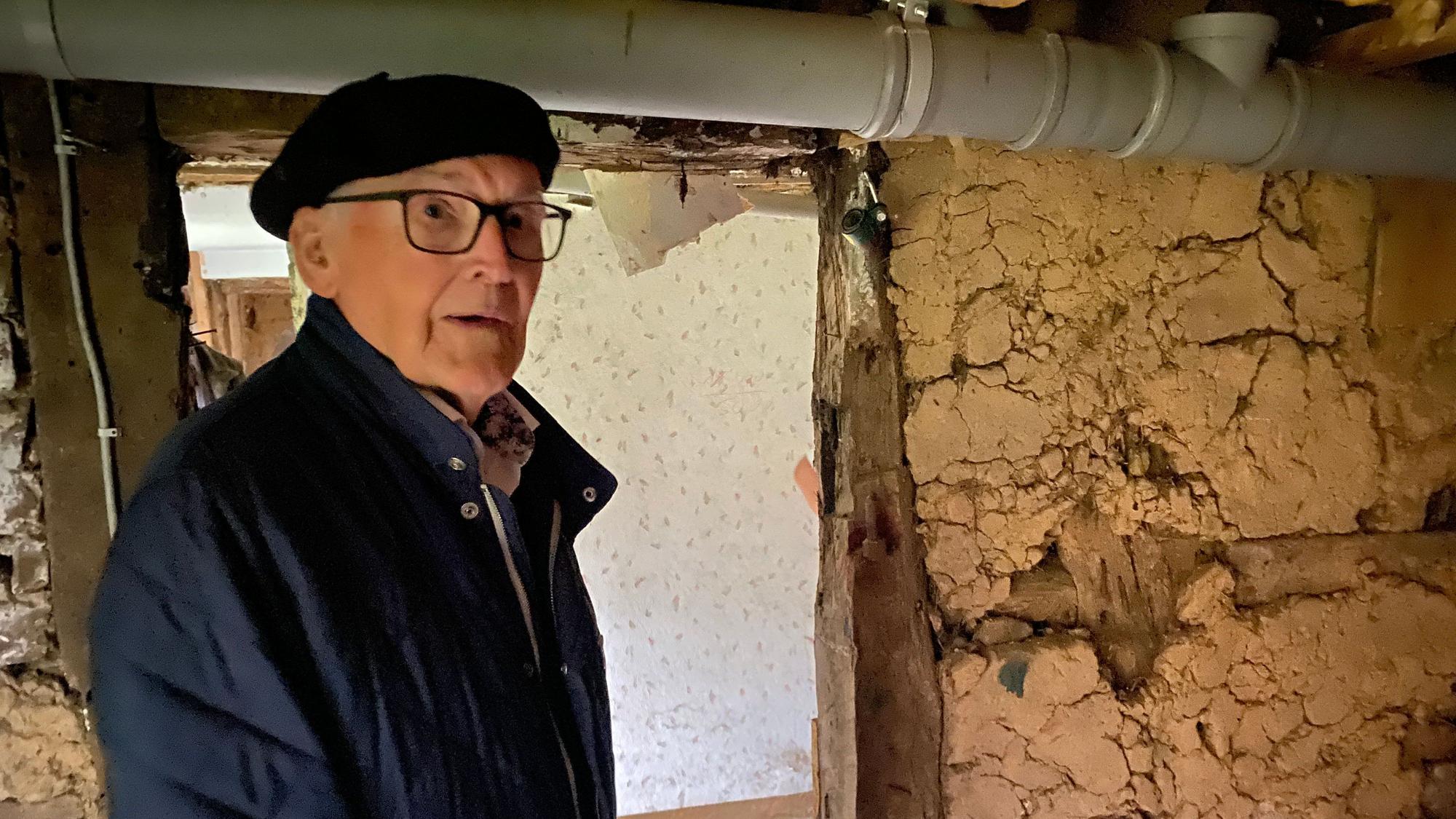 Ein alter Mann vor einer Fachwerkwand mit Lehmgefache.