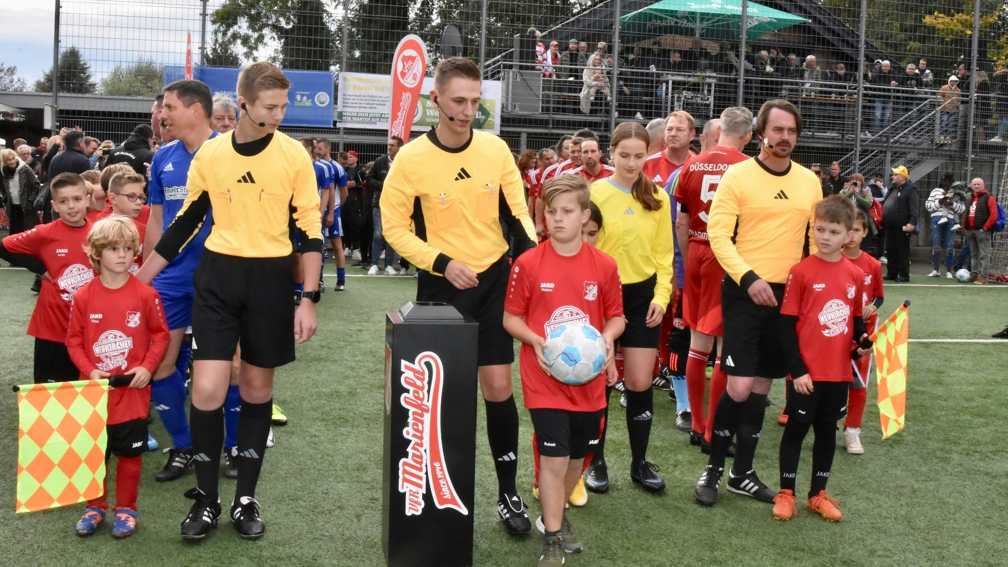 Kinder und Erwachsene in Sportkleidung stehen am Rand eines Fußballplatzes.