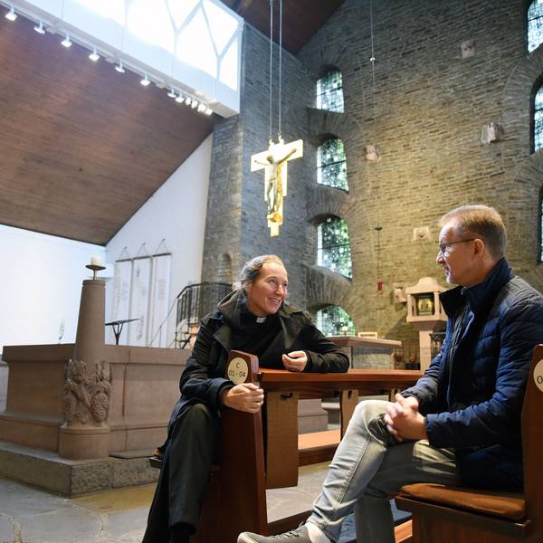 Eine Frau und ein Mann sitzen in den Bänken einer Kirche.