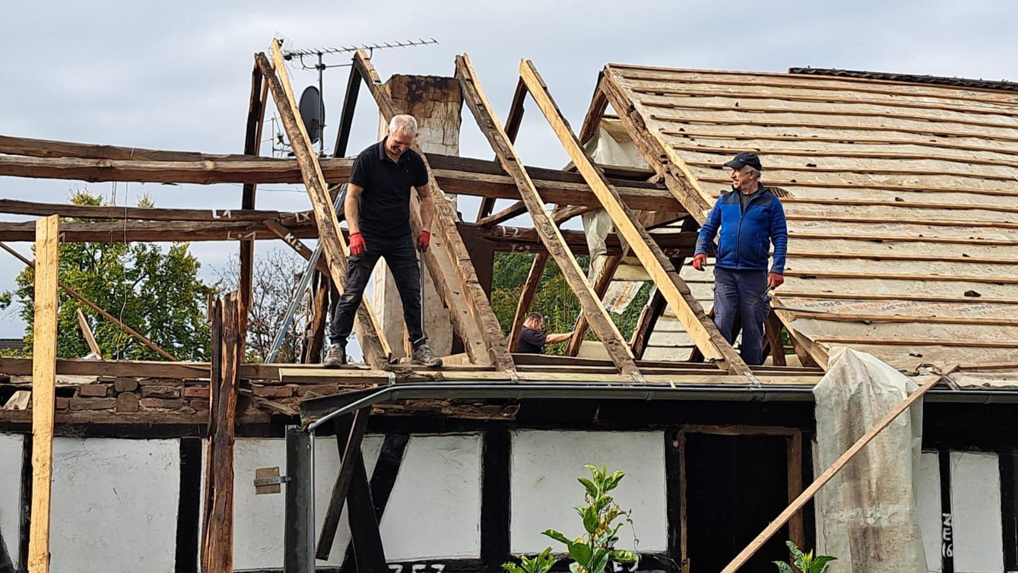 Ein Dachstuhl wird von zwei Männern abgebaut.