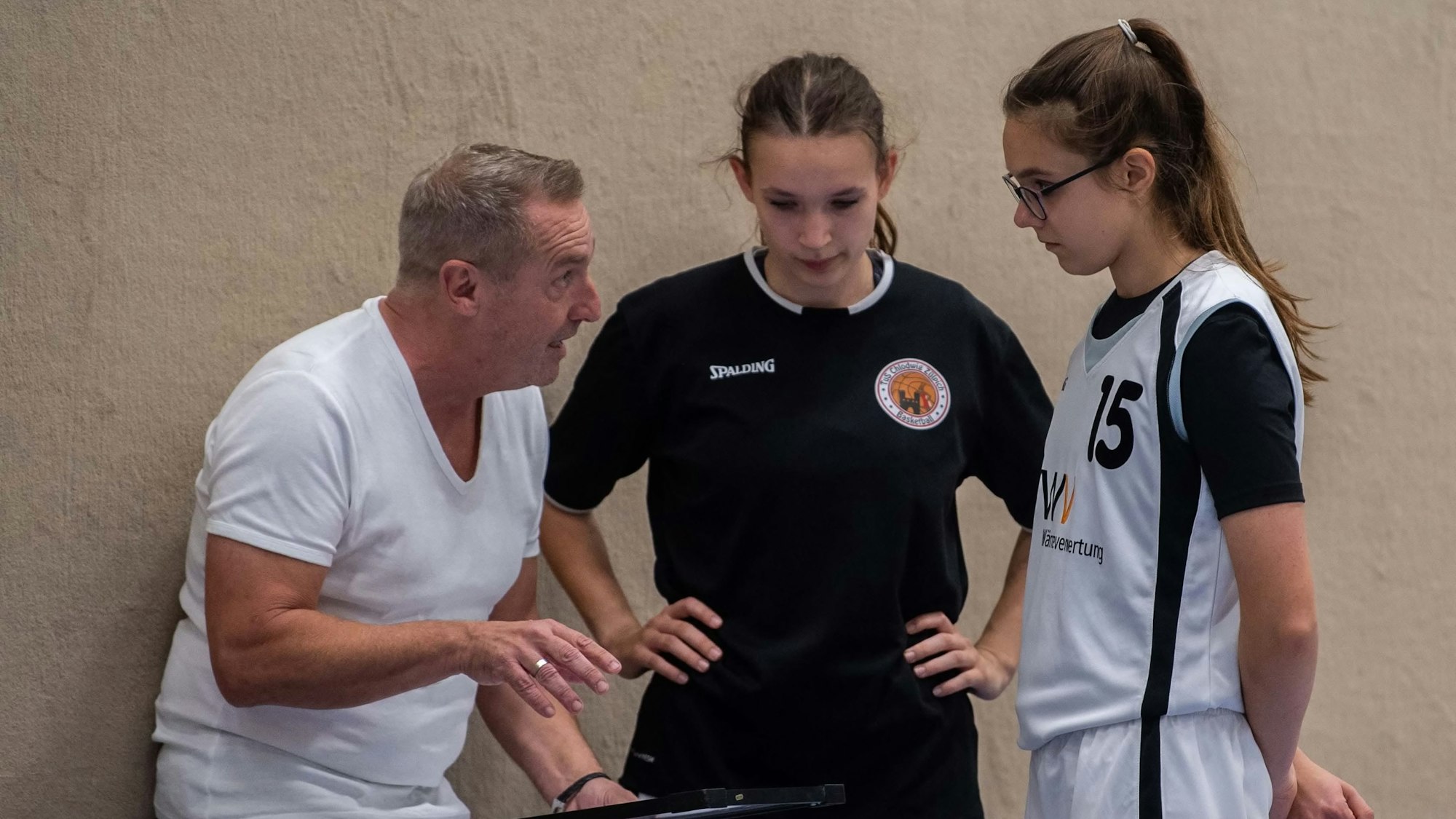 Der Trainer spricht zu zwei Basketballerinnen. Sie hören aufmerksam zu.