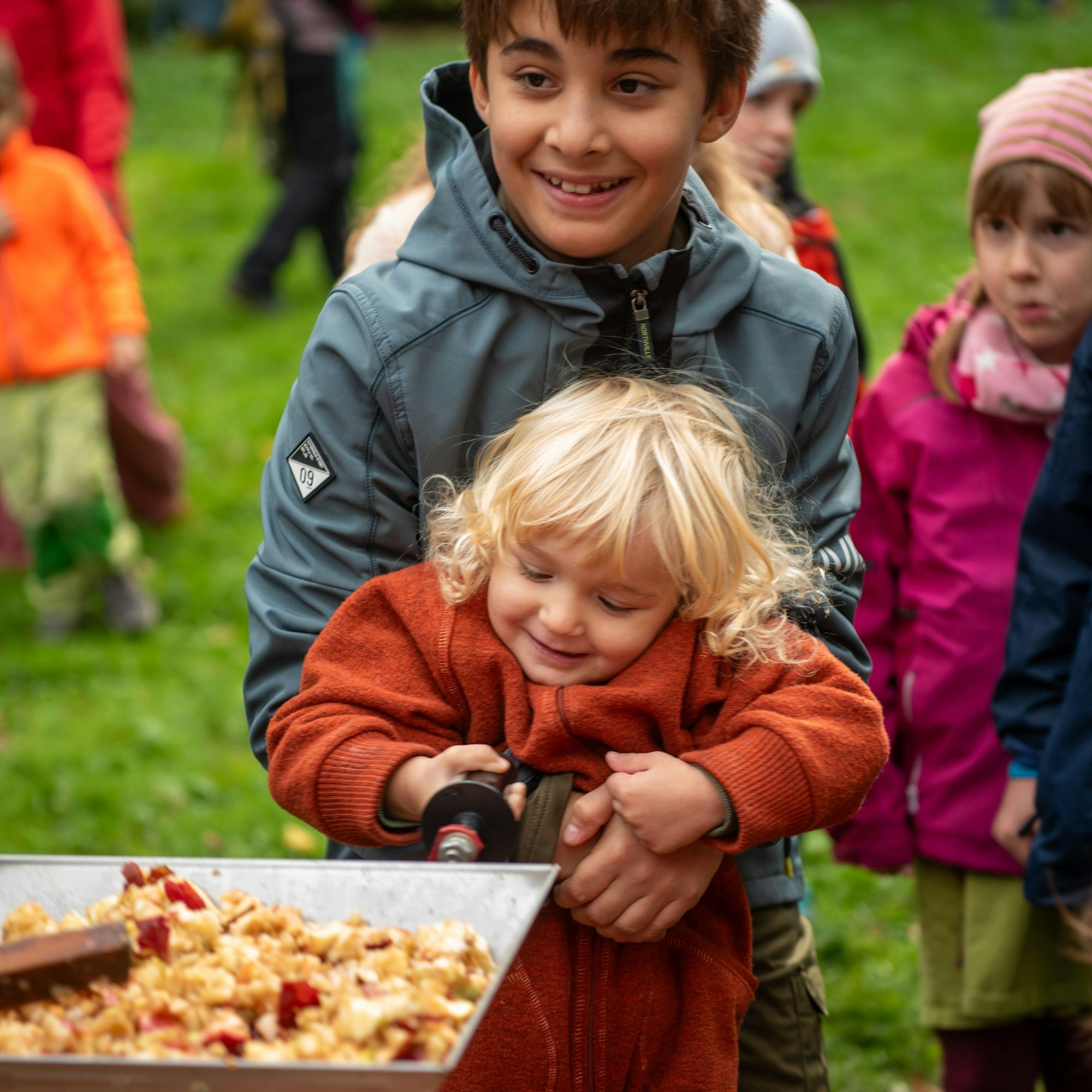Can hebt seinen kleinen Bruder Levent Gülmez hoch, damit er an der Apfelmühle drehen kann.