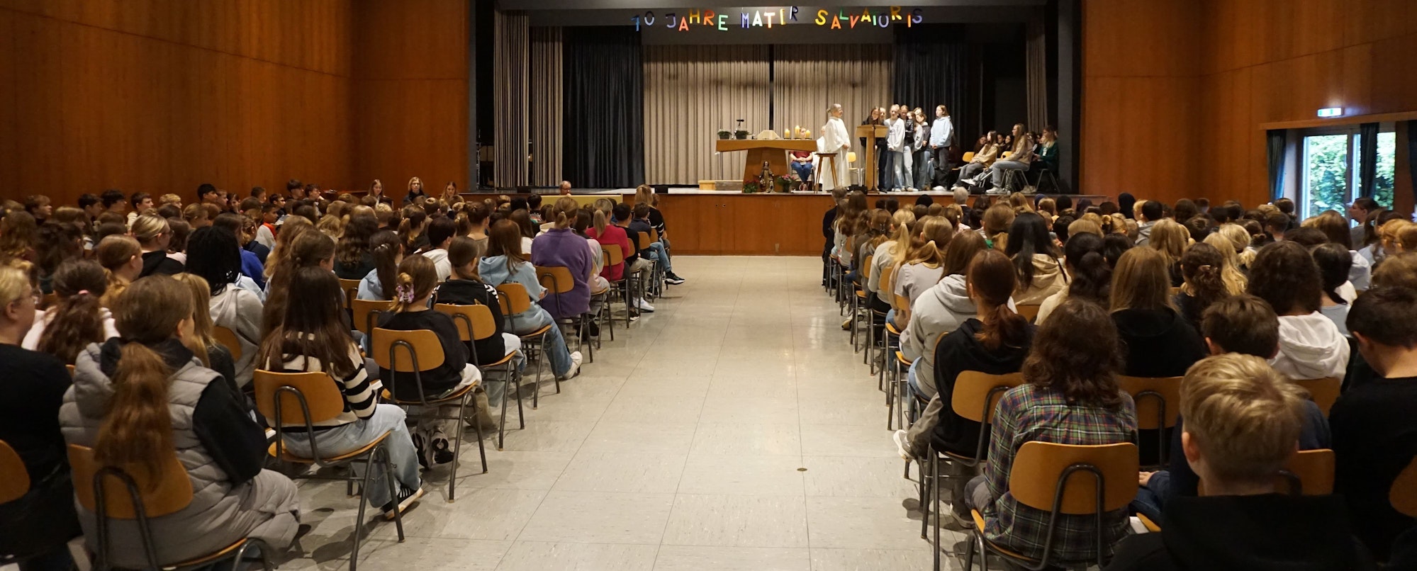 Das Bild zeigt einen Saal voller Schülerinnen und Schüler vor einer Bühne.