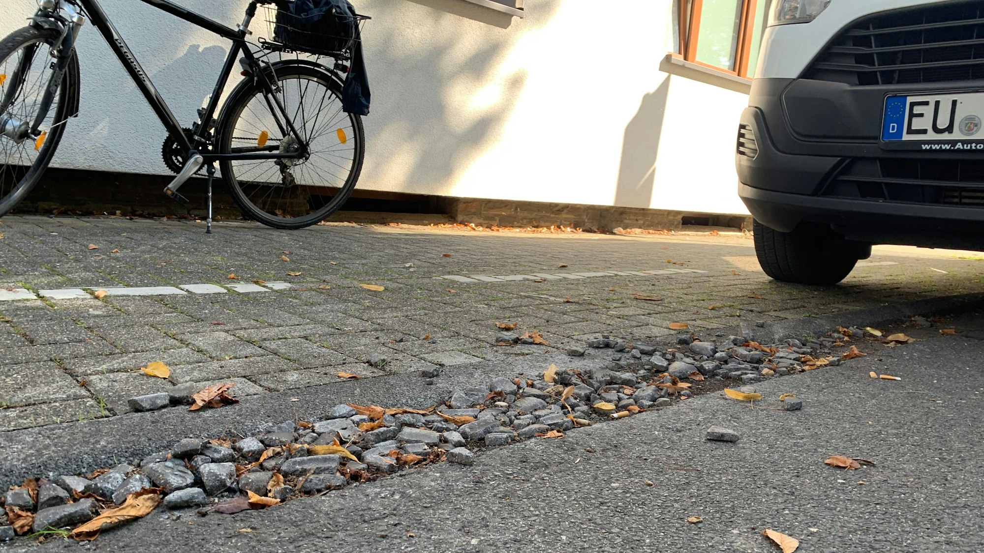 In der Entwässerungsrinne zwischen Fahrbahn und Gehweg liegen Steine, rechts steht ein Auto.