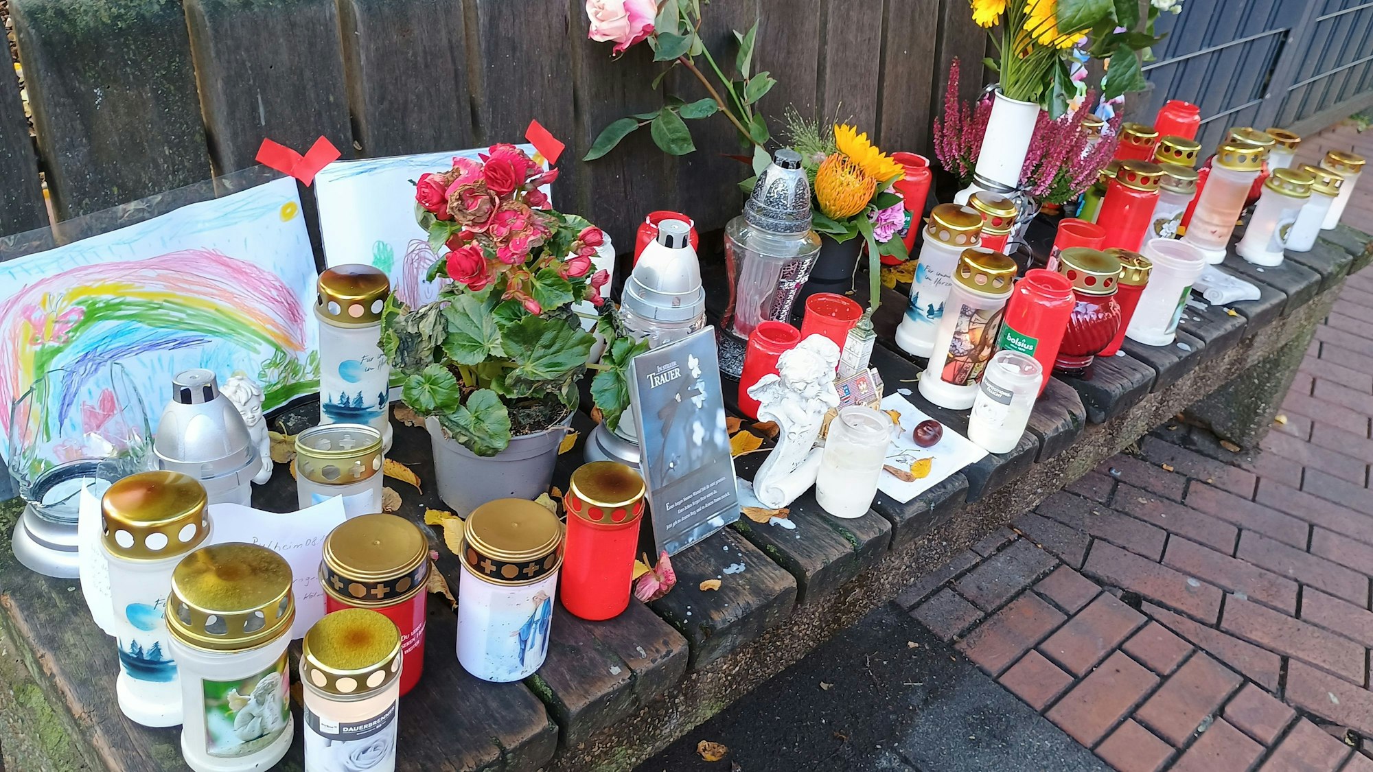 Auf einer Bank haben Pulheimer Anwohner Kerzen, Blumen, Bilder und Briefe abgelegt.