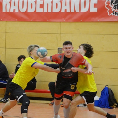 Schmitz, mit dem Ball in der rechten Hand, wird von zwei Abwehrspielern hart bedrängt.