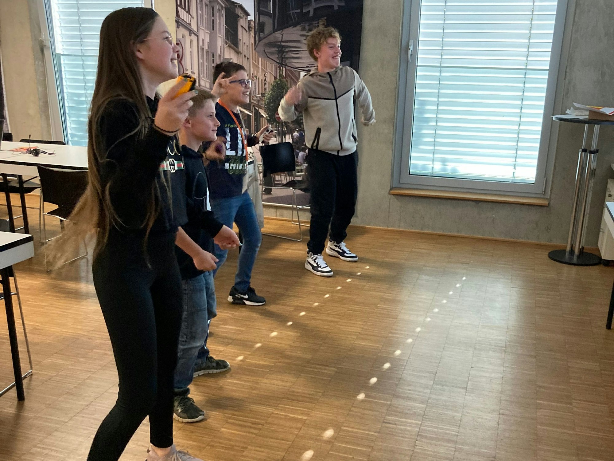 Drei Jungen und ein Mädchen bewegen sich mit Controllern in einem Zimmer.