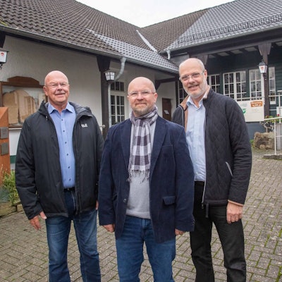 Vor dem Dorfgemeinschaftshaus in Thier stehen drei Männer und schauen in die Kamera.