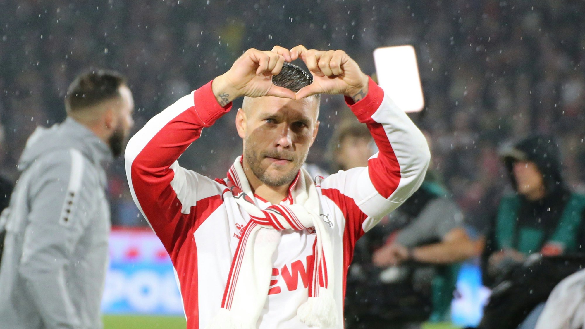 Der Fußballspieler Lukas Podolski steht auf dem Spielfeld und formt mit seinen Fingern ein Herz.