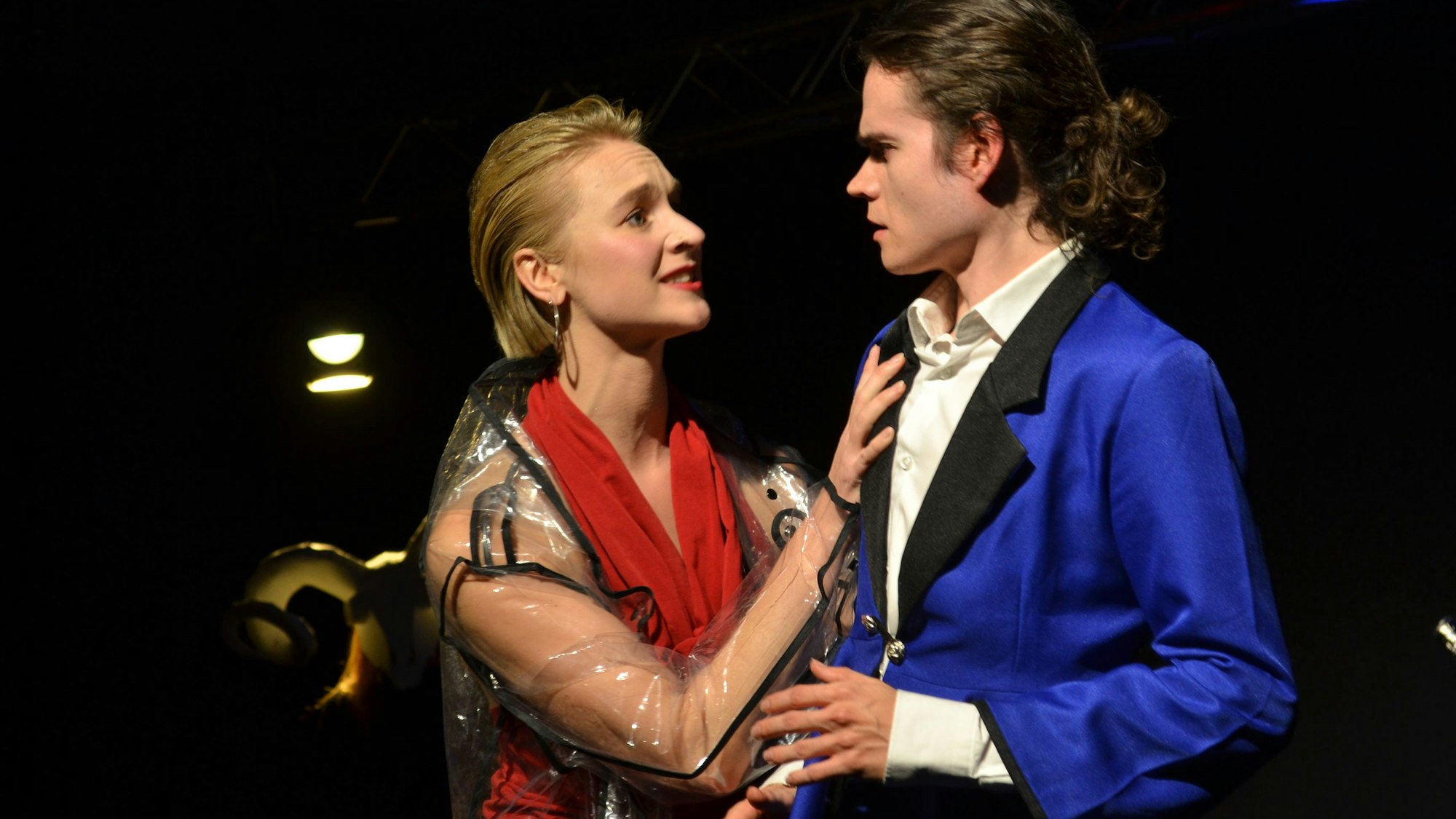 Eine Frau mit rotem Schal und ein Mann im blauen Gehrock in einer Theaterszene.