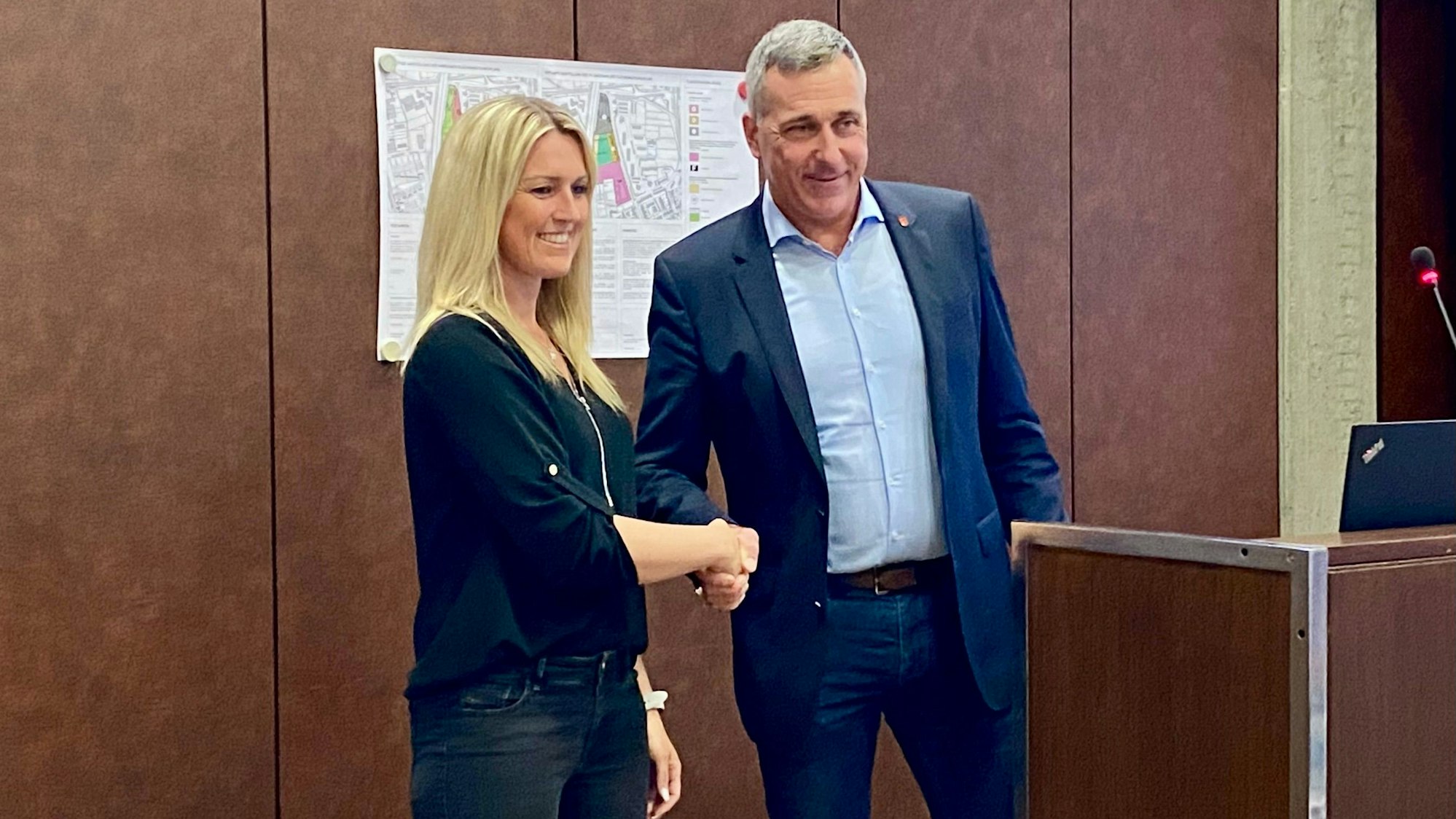 Nicole Jonas schüttelt dem Bürgermeister die Hand und lächelt. Sie hat lange blonde Haare und trägt dunkle Kleidung.