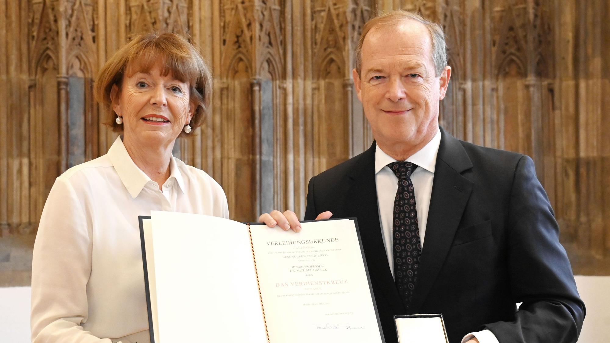 Zu sehen sind Oberbürgermeisterin Henriette Reker und Professor Dr. Michael Hallek, die eine Urkunde halten.