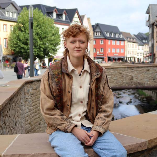 Svea Kirschmeier sitzt auf der Erftmauer in Bad Münstereifel. Sie trägt Jeans und eine braune Lederjacke.
