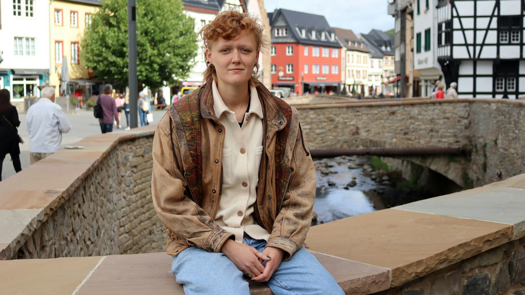 Svea Kirschmeier sitzt auf der Erftmauer in Bad Münstereifel. Sie trägt Jeans und eine braune Lederjacke.