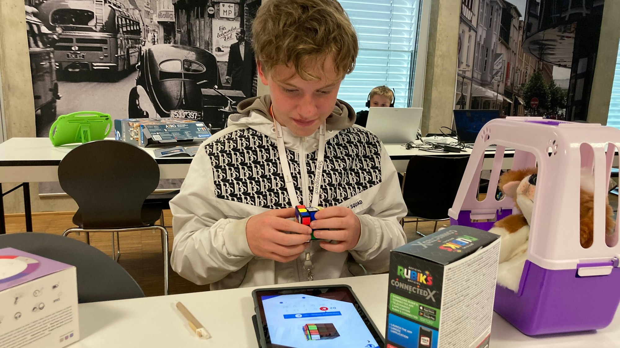 Ein Junge dreht einen Zauberwürfel und schaut dabei auf ein Tablet.